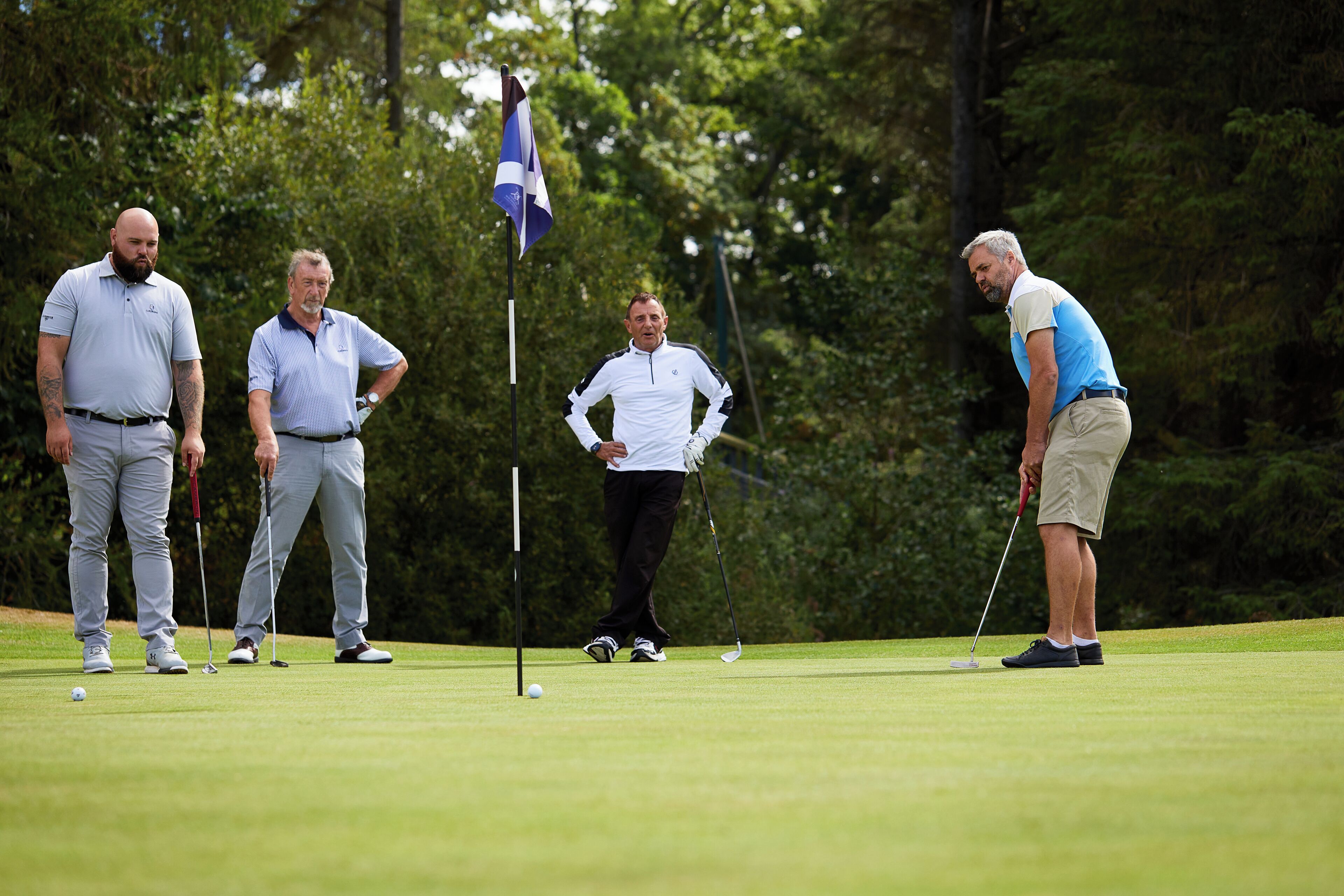 Un groupe de personnes se trouve sur un terrain de golf, avec un mât de drapeau au centre.