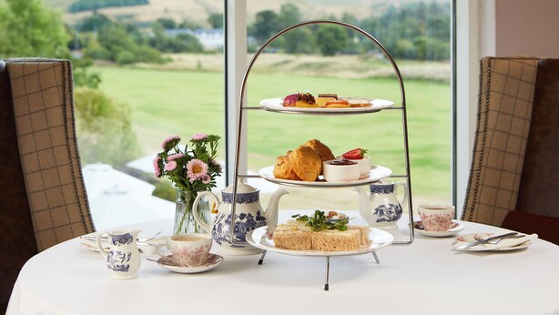 A three-tiered tea service set on a table with a scenic view. - Macdonald Cardrona Hotel, Golf & Spa (Peebles)