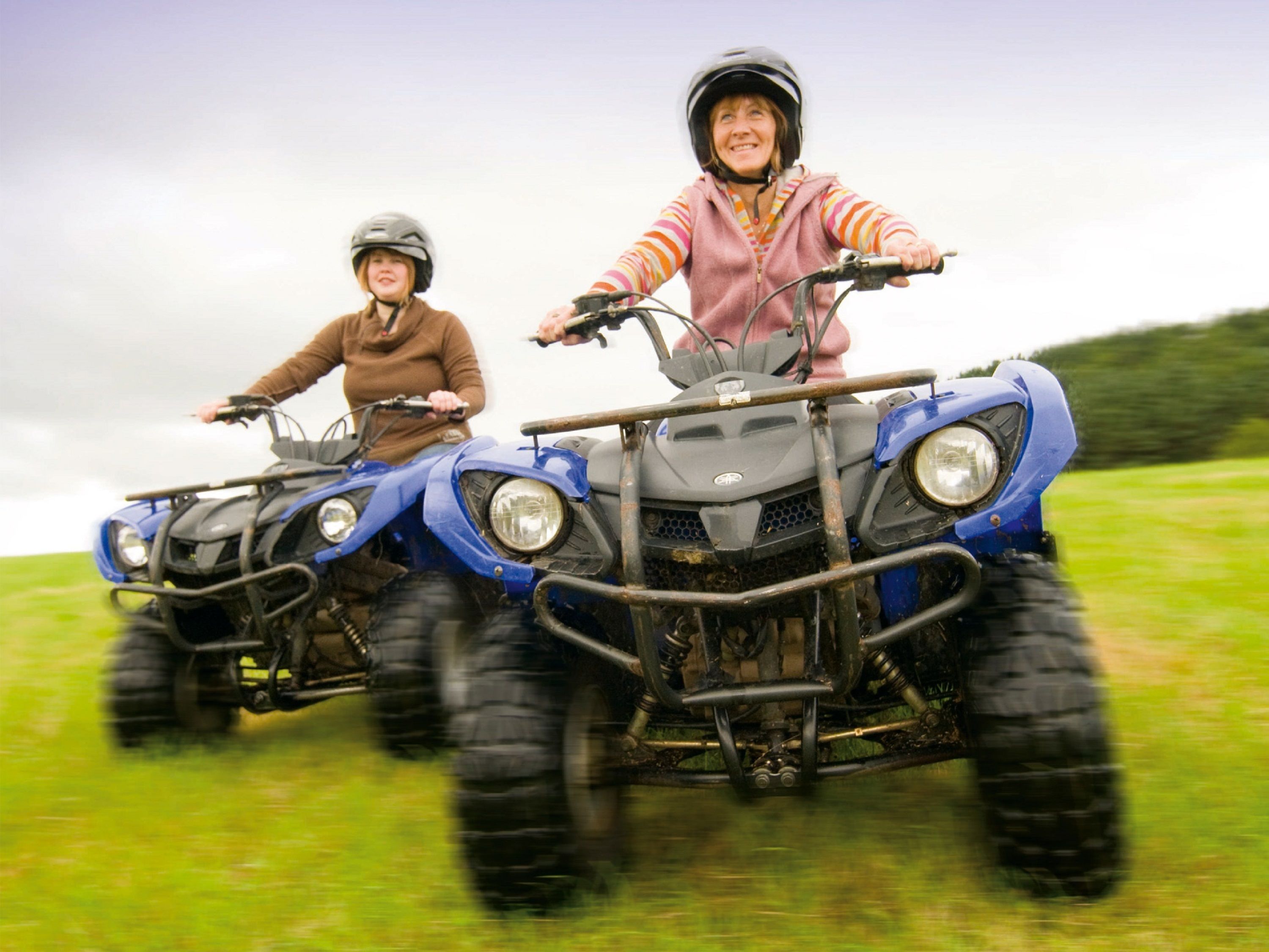 Two people riding an ATV in a grassy field.
