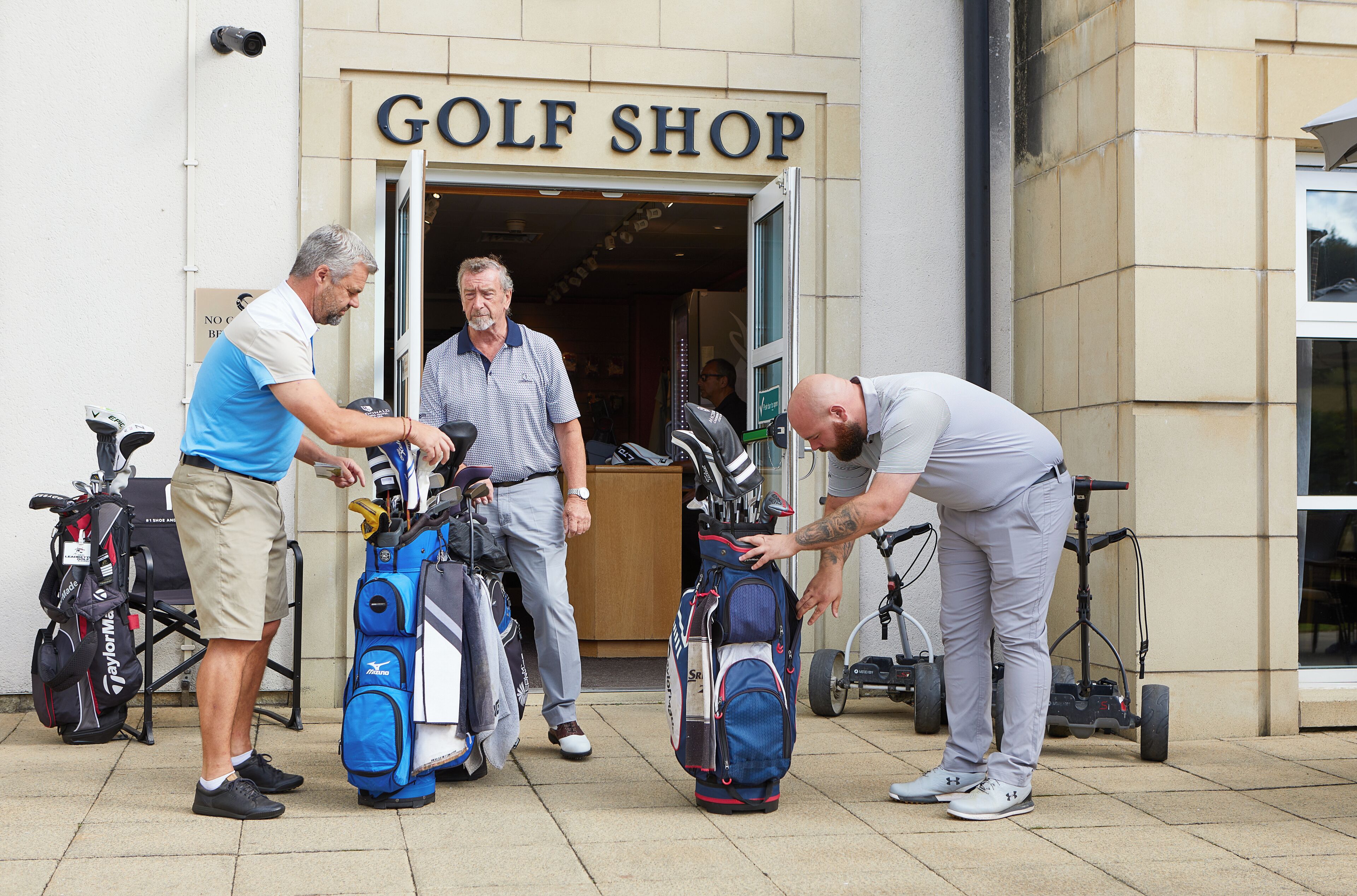 A golf shop entrance with people handling golf bags and a golf cart.