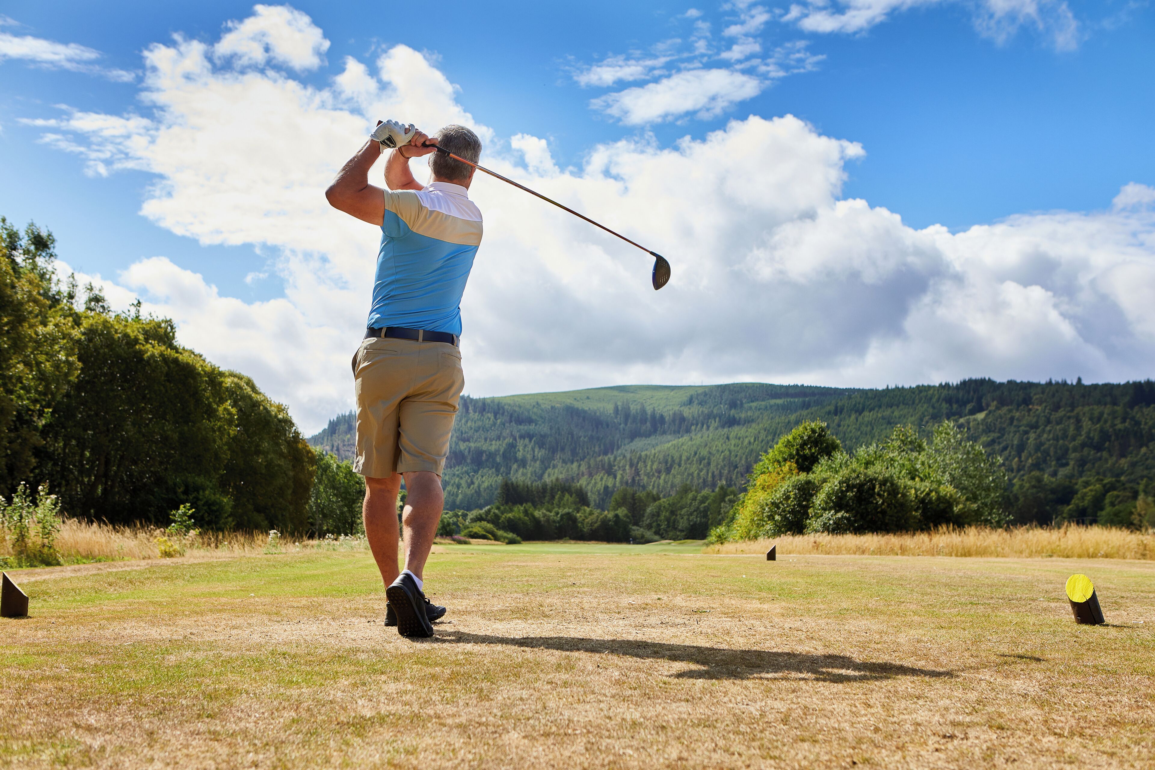 A person playing golf on a sunny day with a clear sky and green hills in the background.