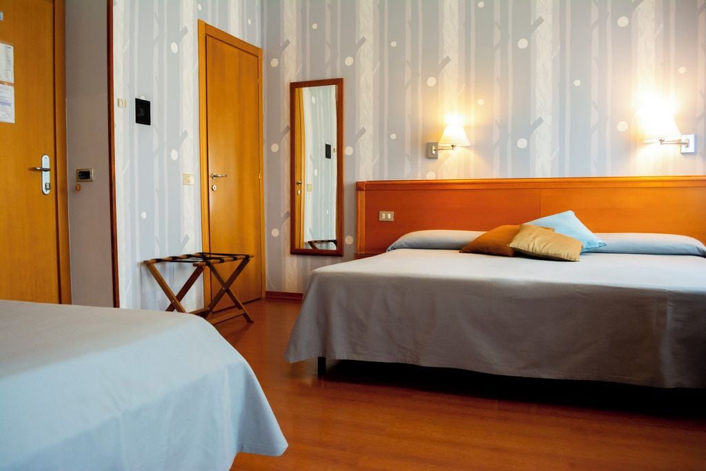A hotel room with two beds, a wooden headboard, and a mirror on the wall.