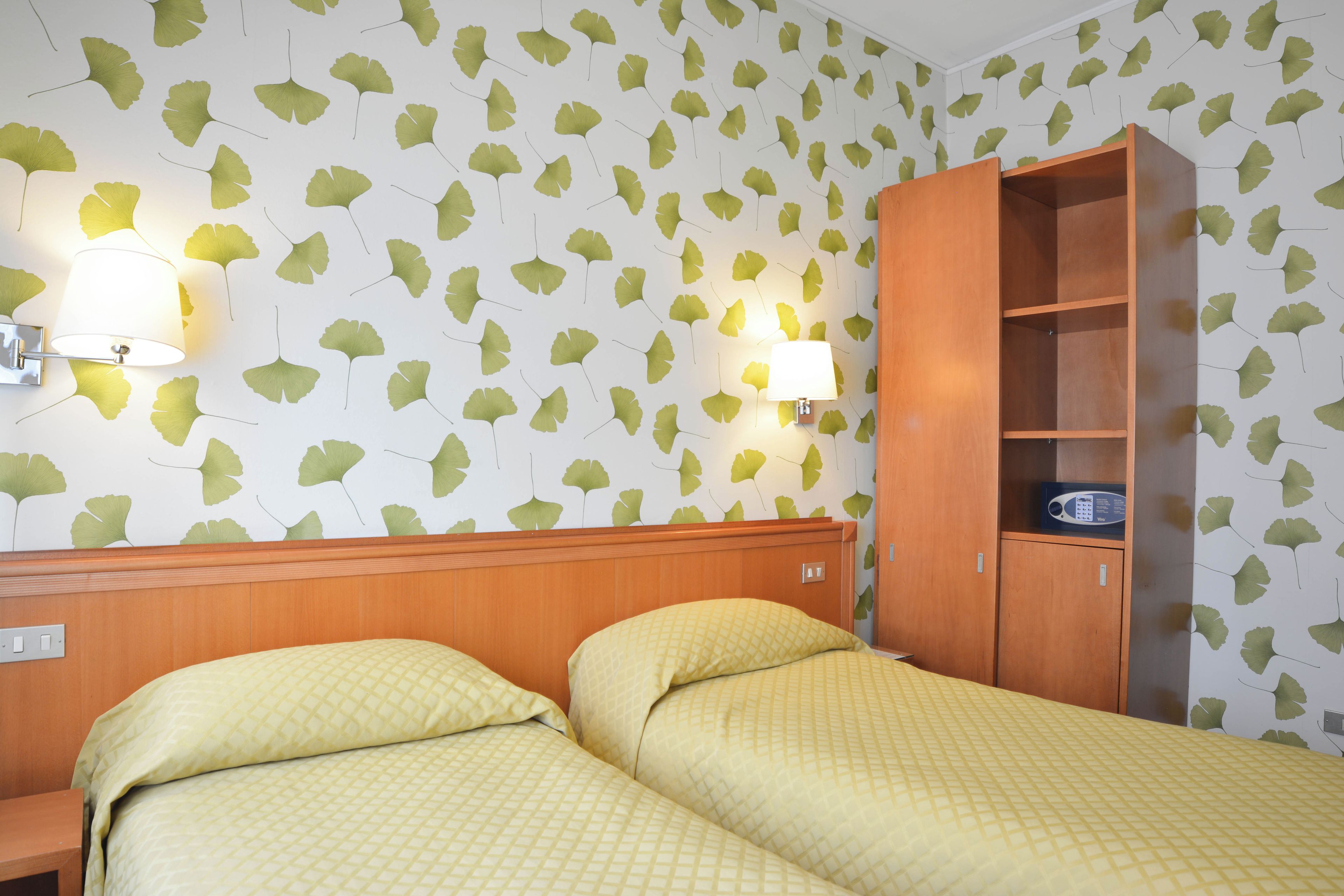 A hotel room with two beds, a wooden wardrobe, and wall-mounted lamps.