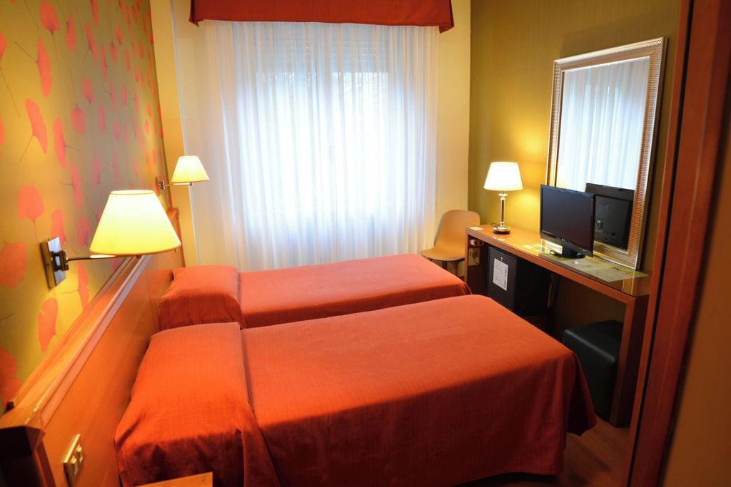A hotel room with two beds, a desk with a computer, and a television.