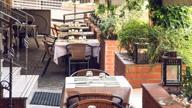 An outdoor dining area with tables set for two, featuring wicker chairs and a brick wall backdrop. - eco Hotel Milano & BioRiso Restaurant (Milan)