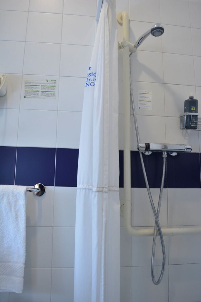 Un baño con ducha, toallero y un cartel en la pared.