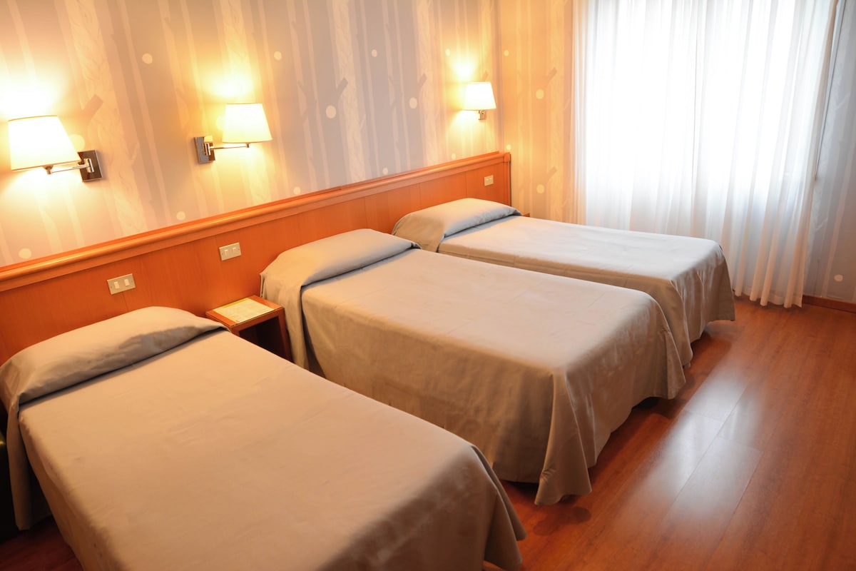 Habitación de hotel con tres camas individuales, cabeceros de madera y lámparas de pared.