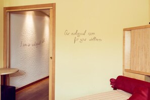 Een kamer met een houten deur, een wand met een wellness boodschap en een rode kussen op een bed.