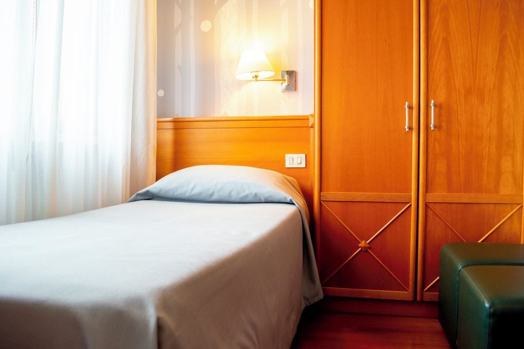 A hotel room with a bed, a nightstand, a wardrobe, and a lamp.