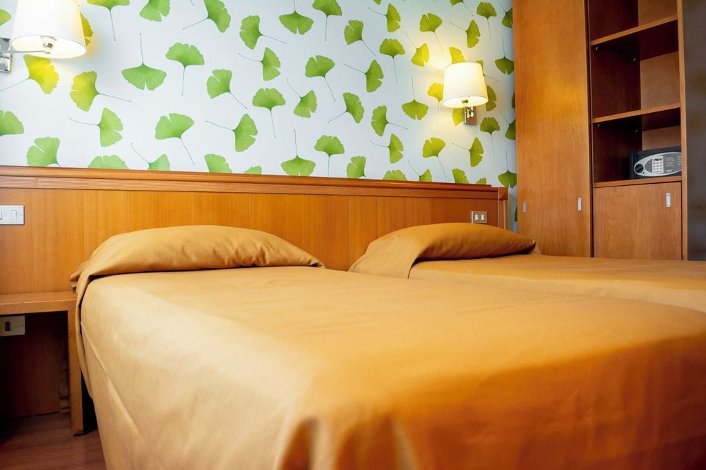 Habitación de hotel con dos camas, cabecero de madera, lámparas de pared y un radio.