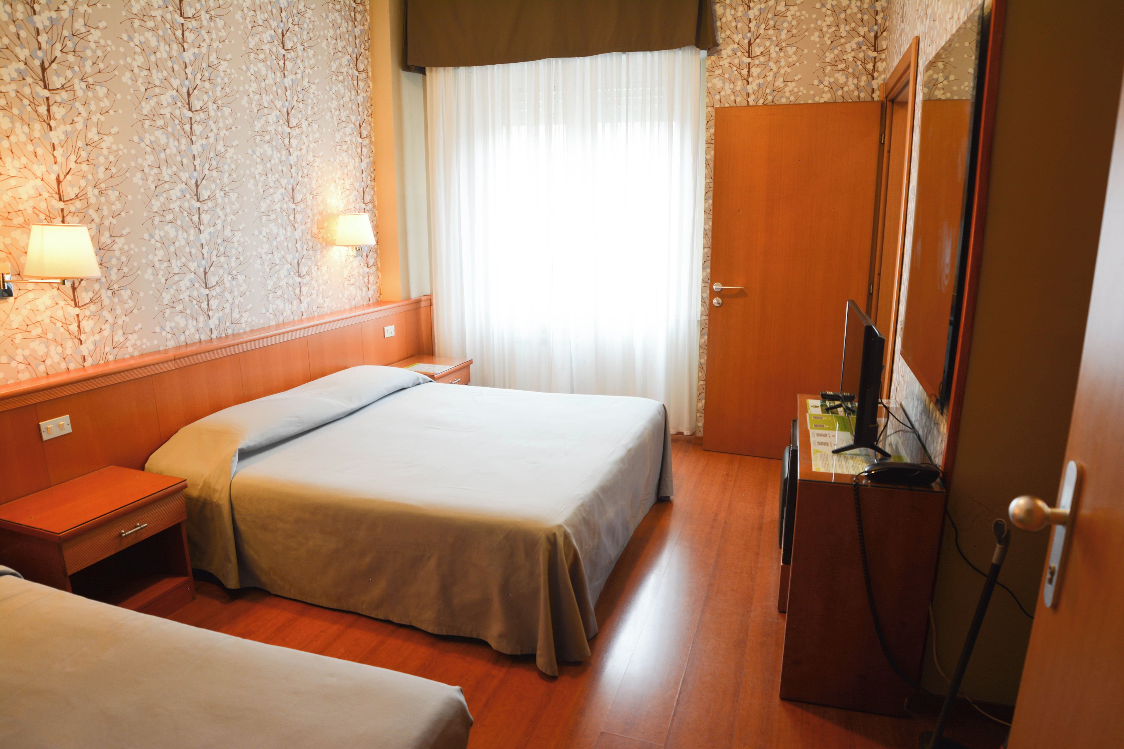 Habitación de hotel con dos camas, un escritorio, un espejo y una ventana con cortinas.