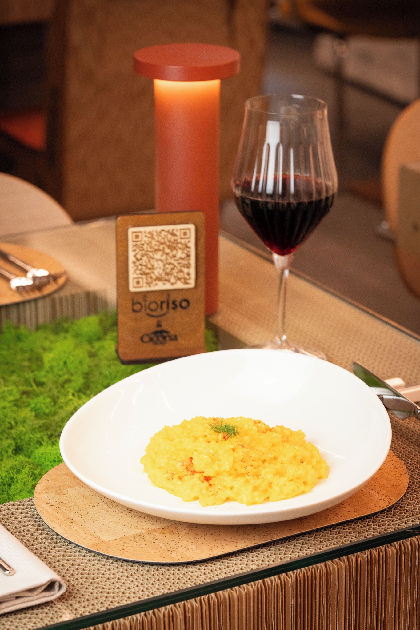A table setting with a plate of food, a glass of red wine, a candle, and a QR code sign.