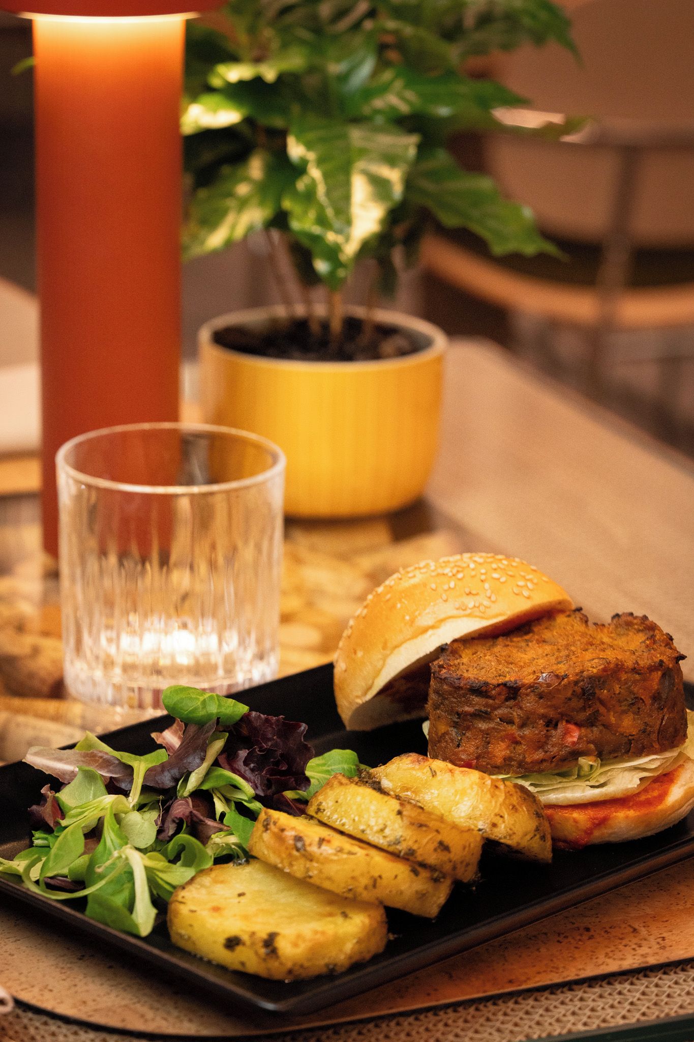 A meal with a burger, fries, and salad on a plate, a glass of water, and a candle.
