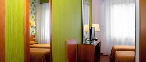 A hotel room with two beds, a desk with a computer, a mirror, and a window with curtains.