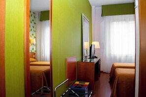 Een hotelkamer met twee bedden, een bureau met een computer, een spiegel en een raam met gordijnen.