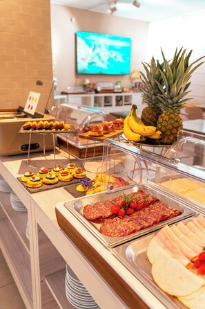 Un bufé con diversas opciones de comida, incluyendo carnes cortadas, frutas y pasteles.