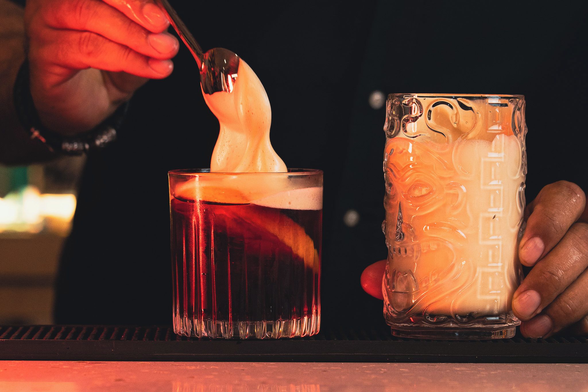 A person holding a glass with a frothy drink and a spoon, and another glass with a different design.