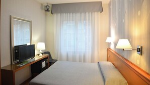 A hotel room with a bed, a desk with a TV, a lamp, and a window with curtains. - eco Hotel Milano & BioRiso Restaurant (Milan)