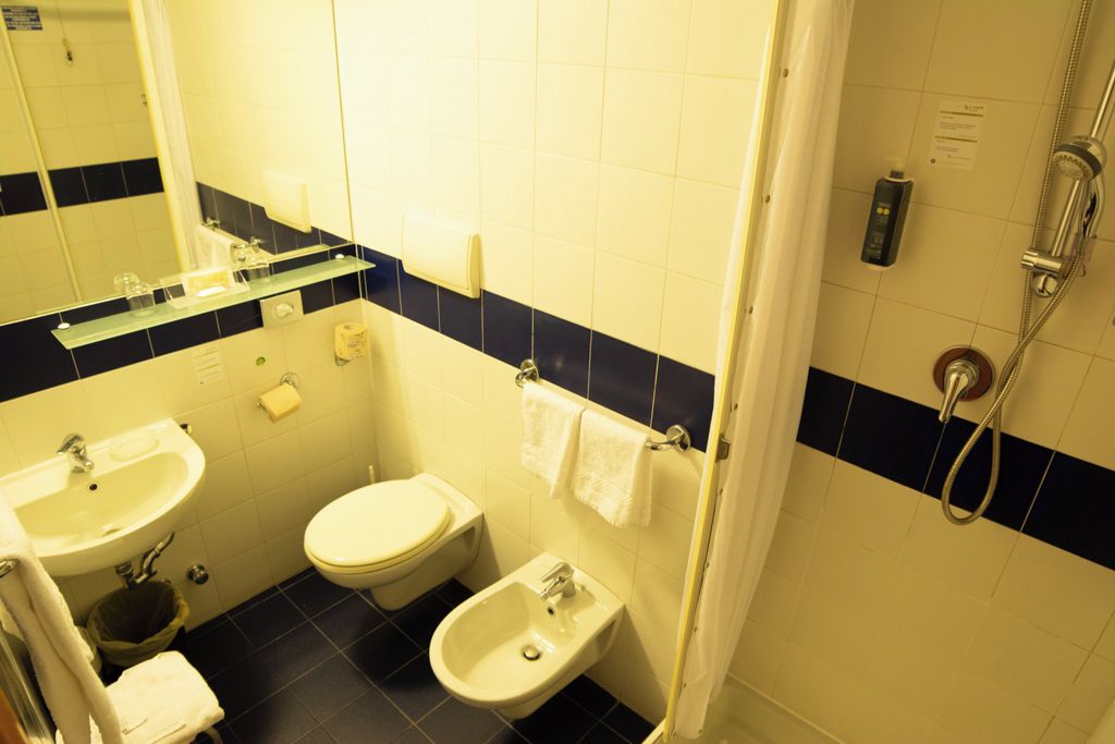 Een kleine badkamer met een wastafel, toilet, toiletbril en een douchehoek.