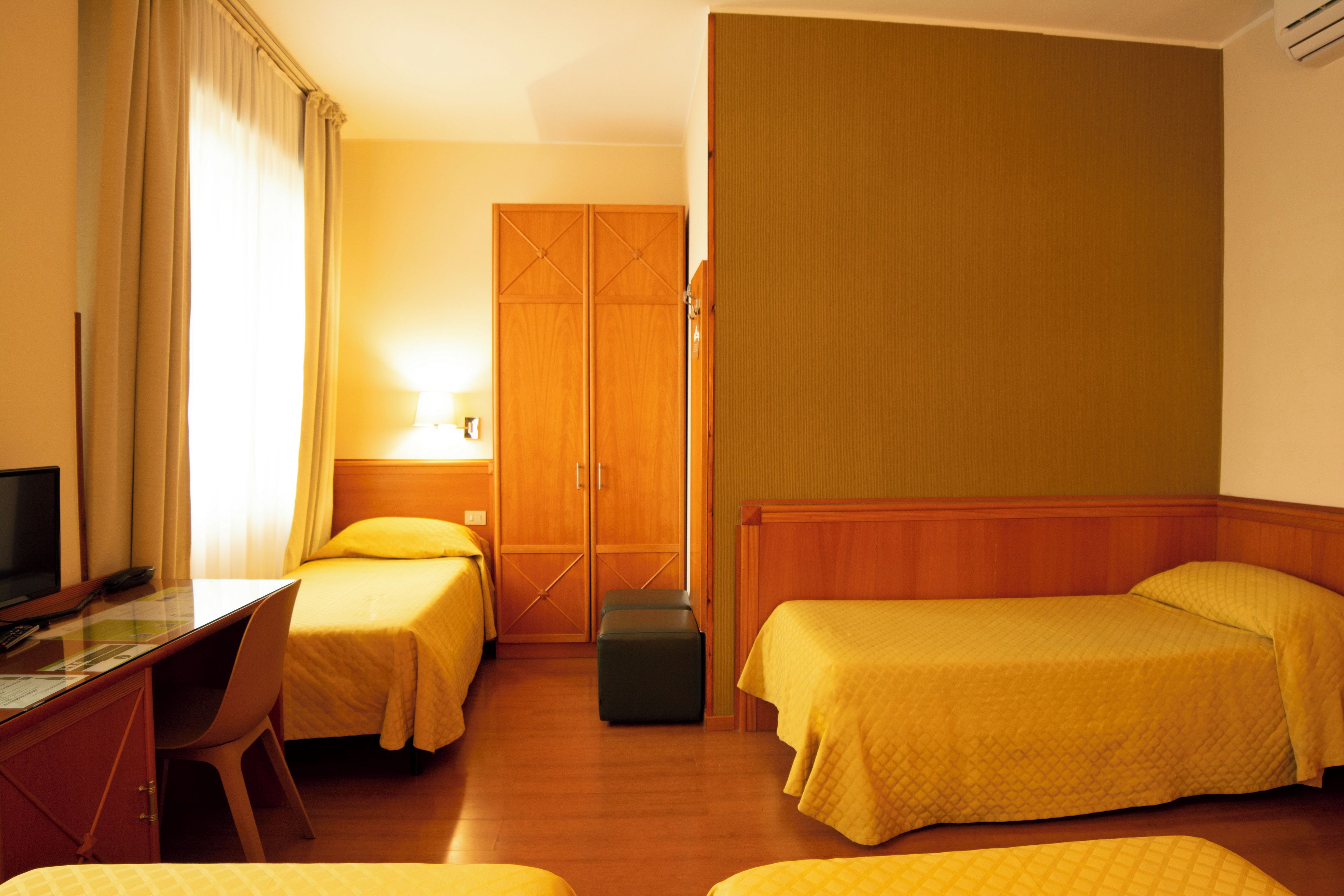 A hotel room with two beds, a desk, a chair, a television, and a wardrobe.