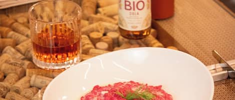 Un piatto di cibo, una bottiglia di BIO cola, un bicchiere di liquido ambrato e una candela su un tavolo con dei tappi di sughero.