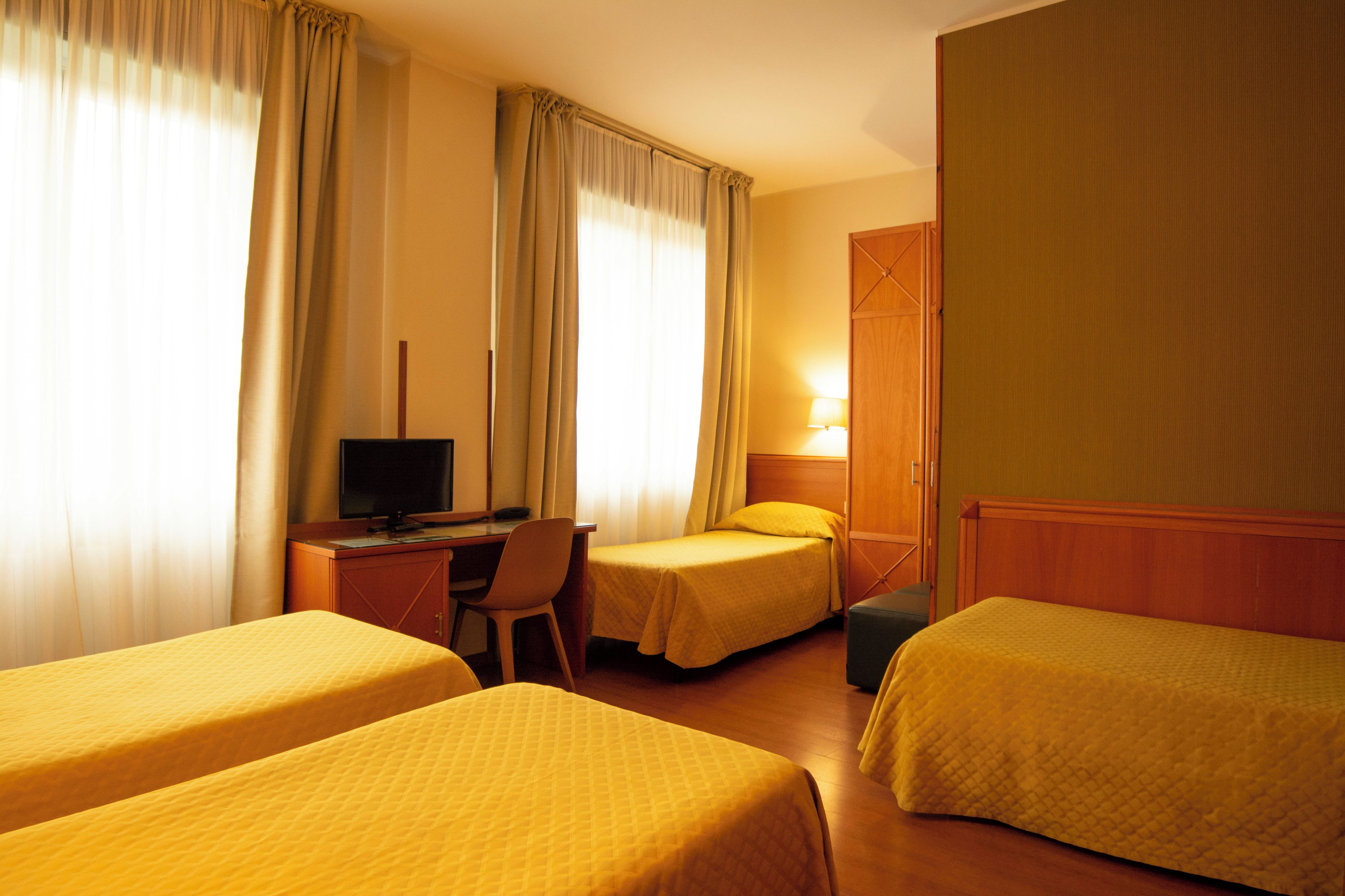 Ein Hotelzimmer mit zwei Betten, einem Schreibtisch, einem Fernseher und einem Kleiderschrank.