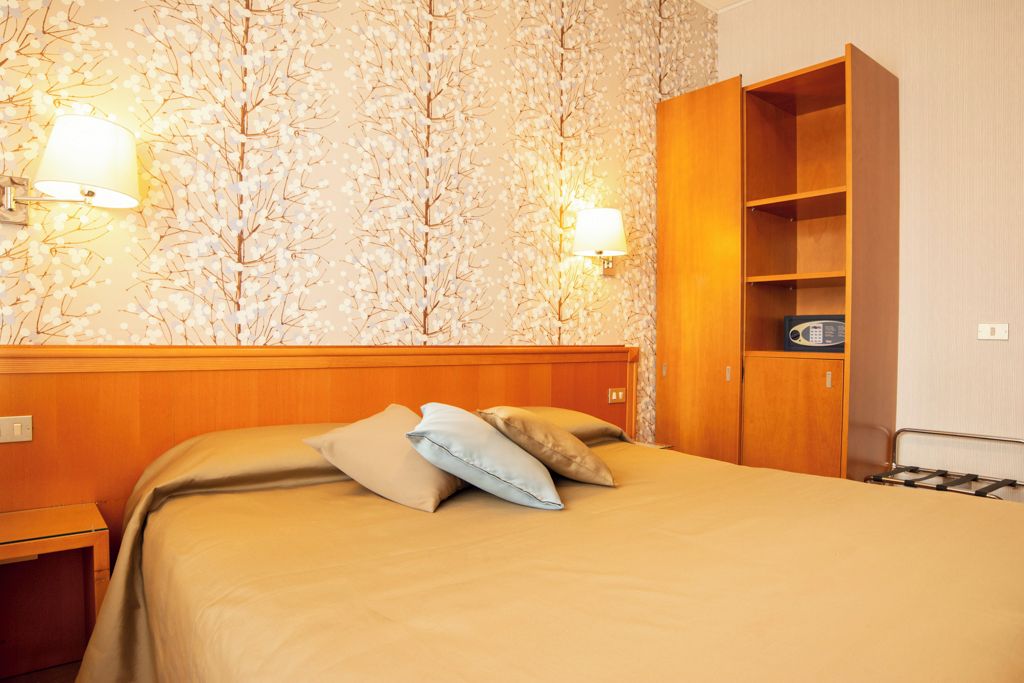 Ein Hotelzimmer mit einem Bett, zwei Wandlampen, einem Kleiderschrank und einem kleinen Tisch.