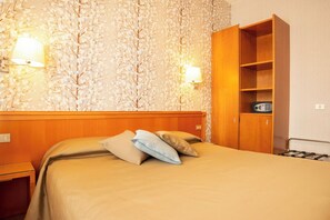 Habitació d'hotel amb llit, dues làmpades penjades a la paret, un armari i una taula petita.