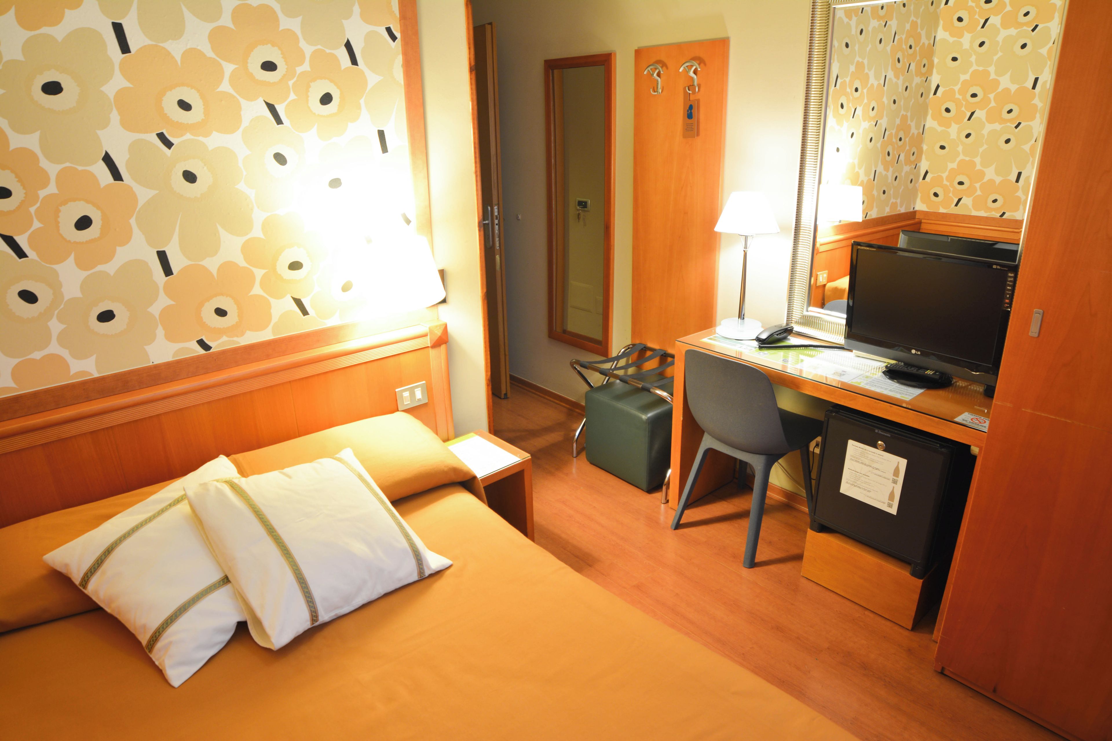 Ein Hotelzimmer mit Bett, Schreibtisch mit Computer, Stuhl, Koffer und Spiegel.