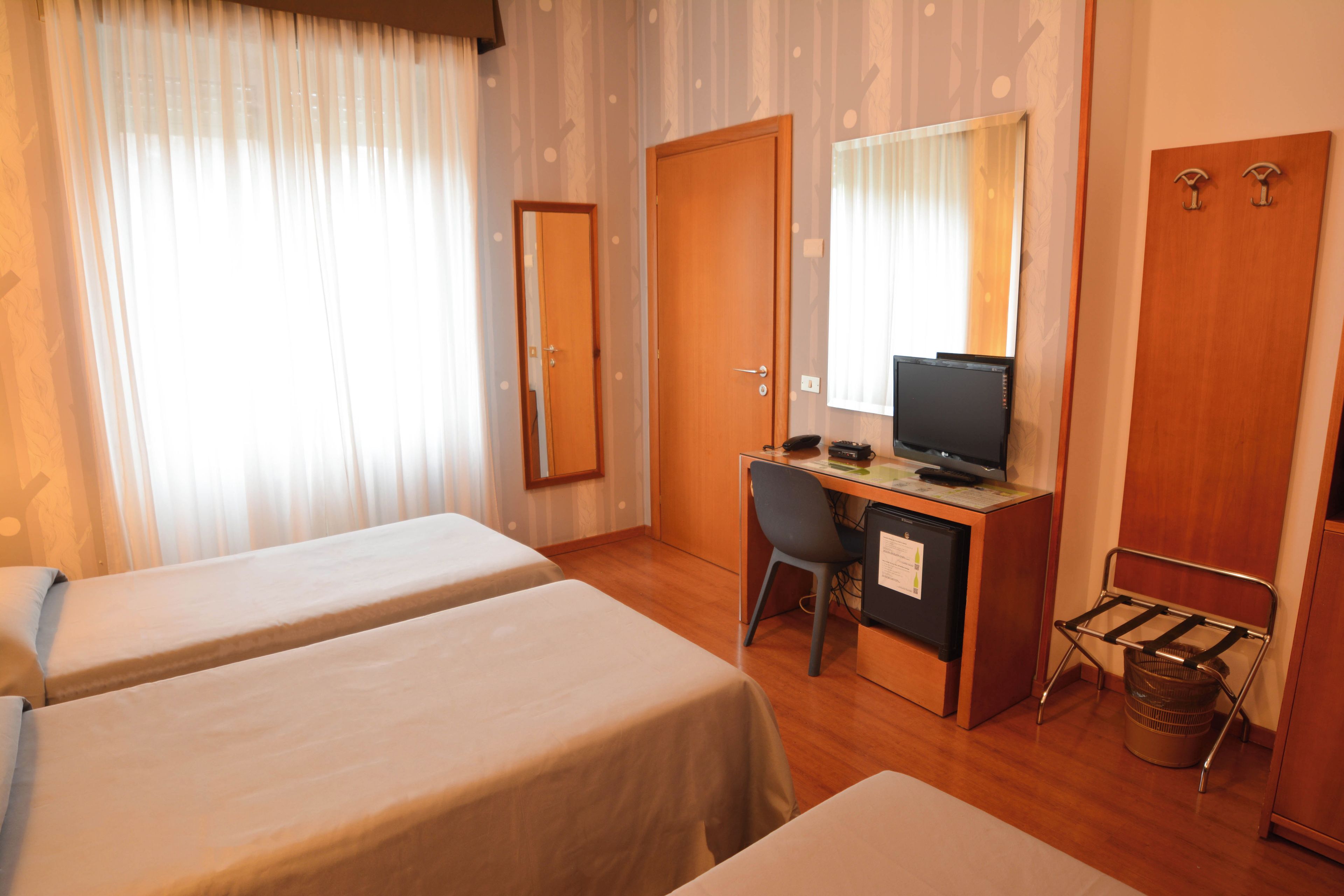 A hotel room with two single beds, a desk with a computer, a chair, and a television.