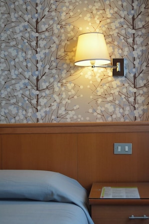 Une chambre d’hôtel avec un lit, une table de chevet, une lampe et un mur orné d’un motif représentant un arbre.