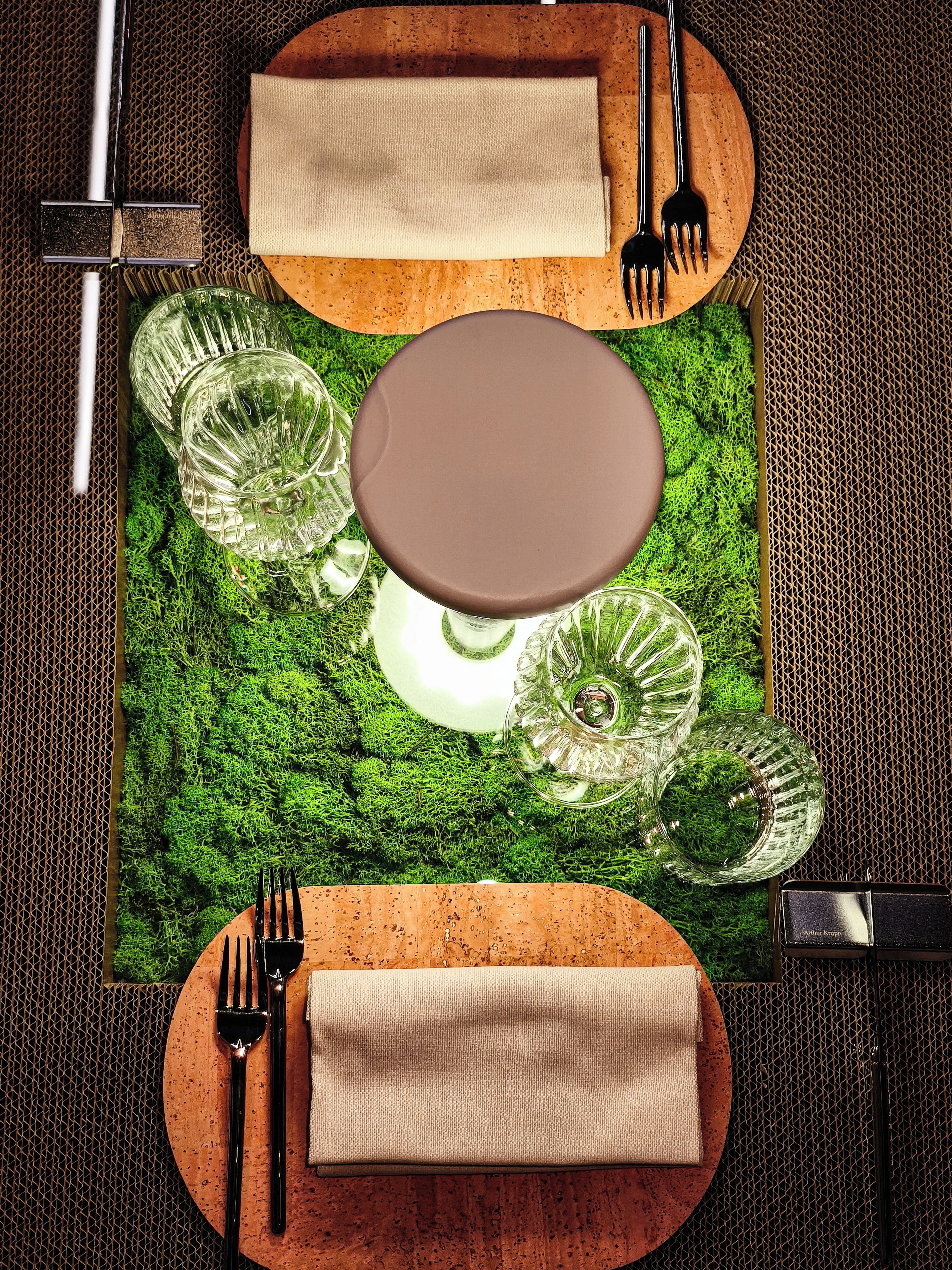 Une table dressée avec un set de table marron, de la verrerie transparente et une serviette beige pliée.