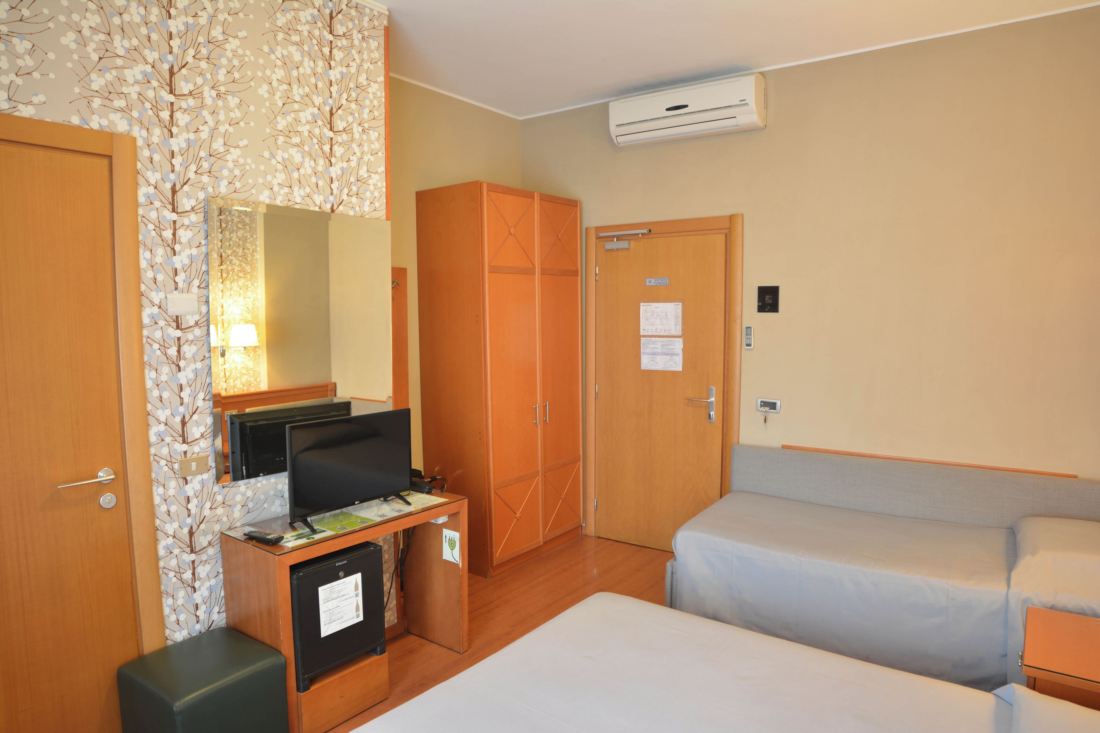 Une chambre d’hôtel équipée d’un lit, d’un bureau avec un ordinateur, d’une armoire et d’un appareil de climatisation.