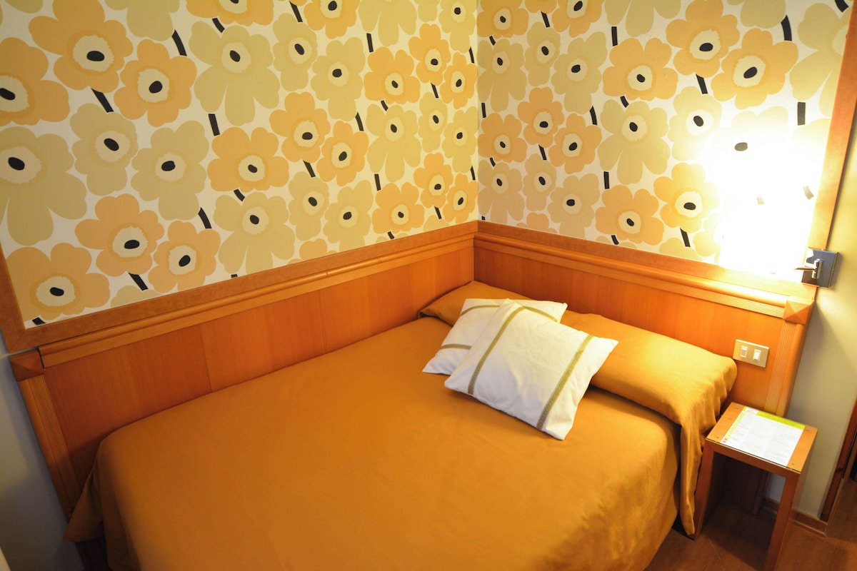 Una habitación de hotel con una cama, una mesita de noche y una pared con estampado floral.