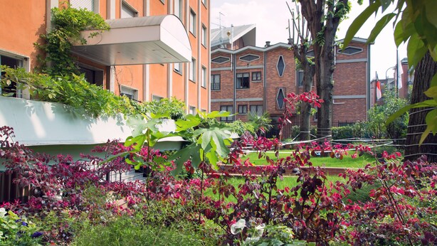 A garden with various plants and flowers, a brick building, and a white structure with a sloped roof. - eco Hotel Milano & BioRiso Restaurant (Milan)