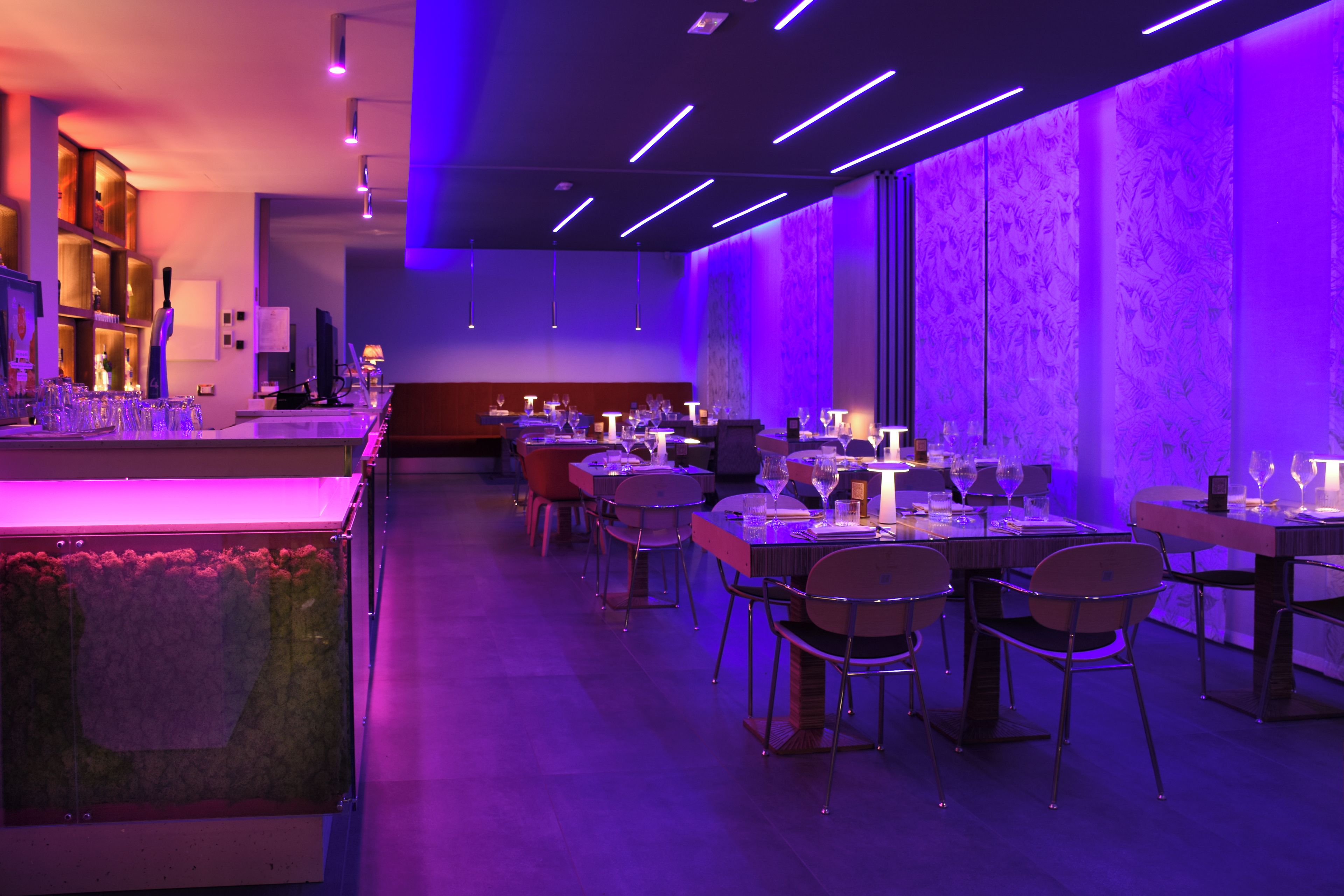 A modern restaurant interior with tables and chairs, a bar area, and a patterned wall.