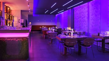 A modern restaurant interior with tables and chairs, a bar area, and a patterned wall.