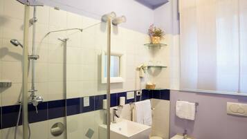 Een badkamer met een douchecabine van glas, een witte wastafel en een toilet.