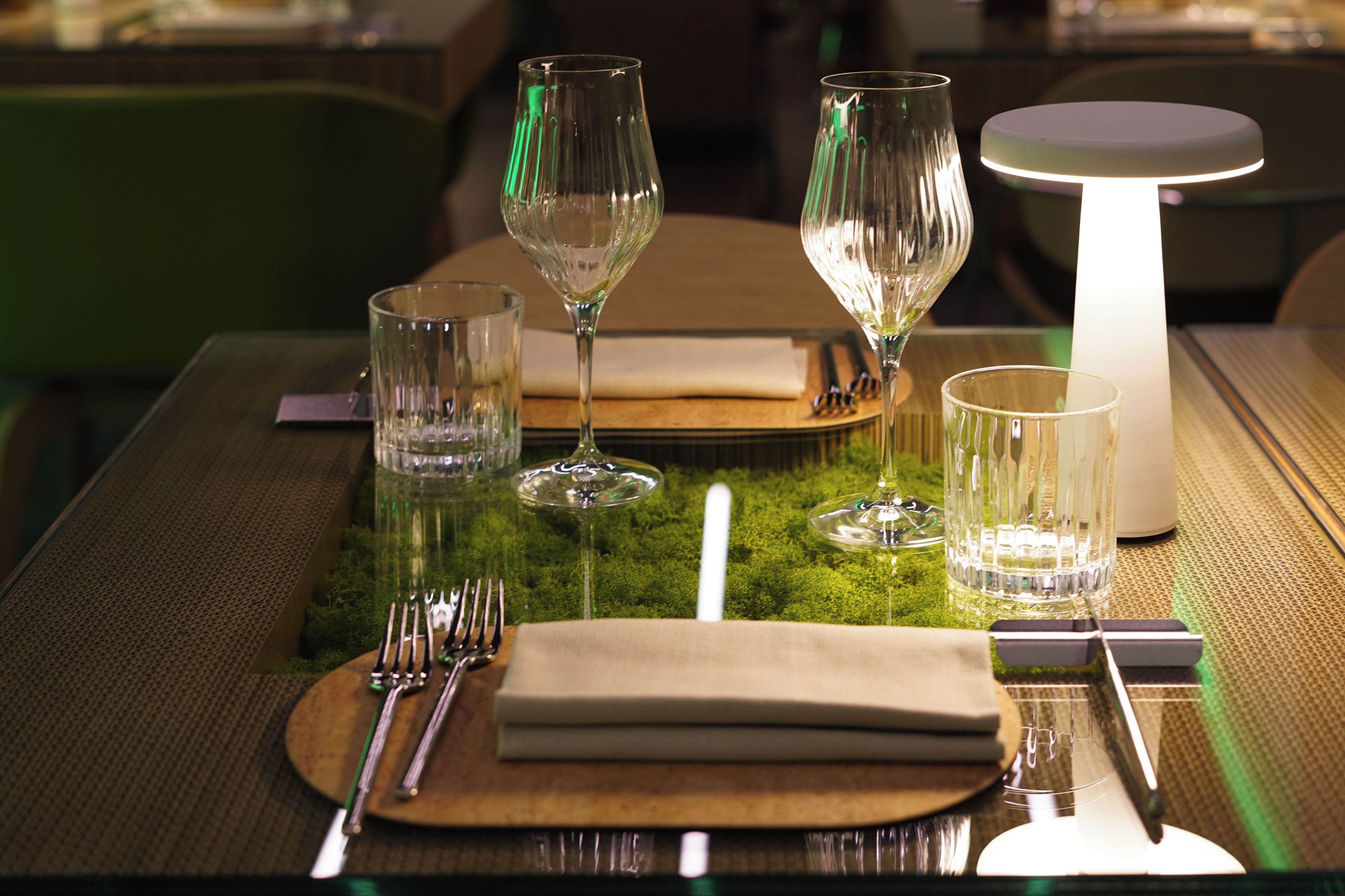 A table set for dining with clear glassware, a candle, and a modern lamp.