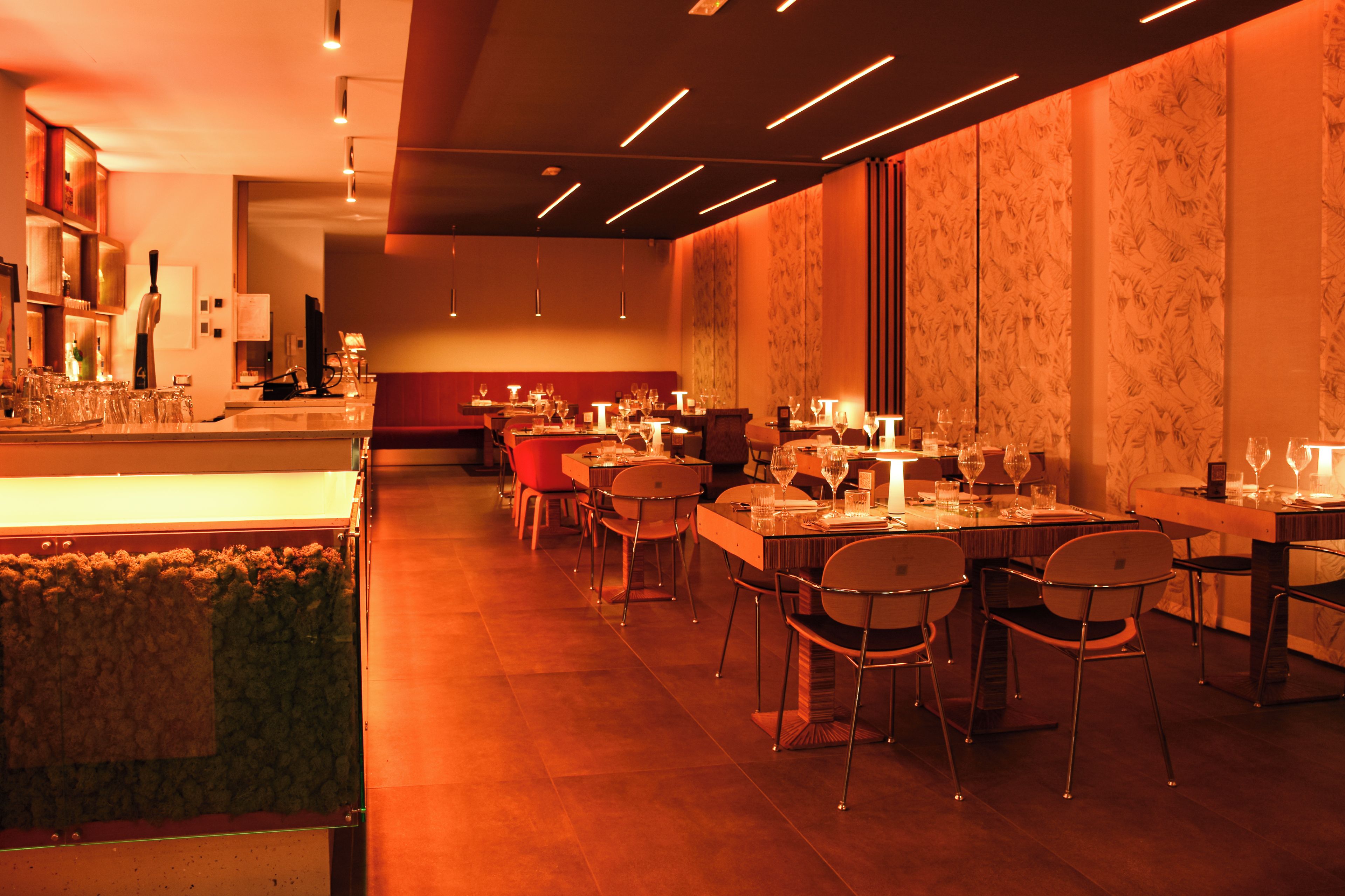 A restaurant interior with multiple tables and chairs, a bar area, and a patterned wall.