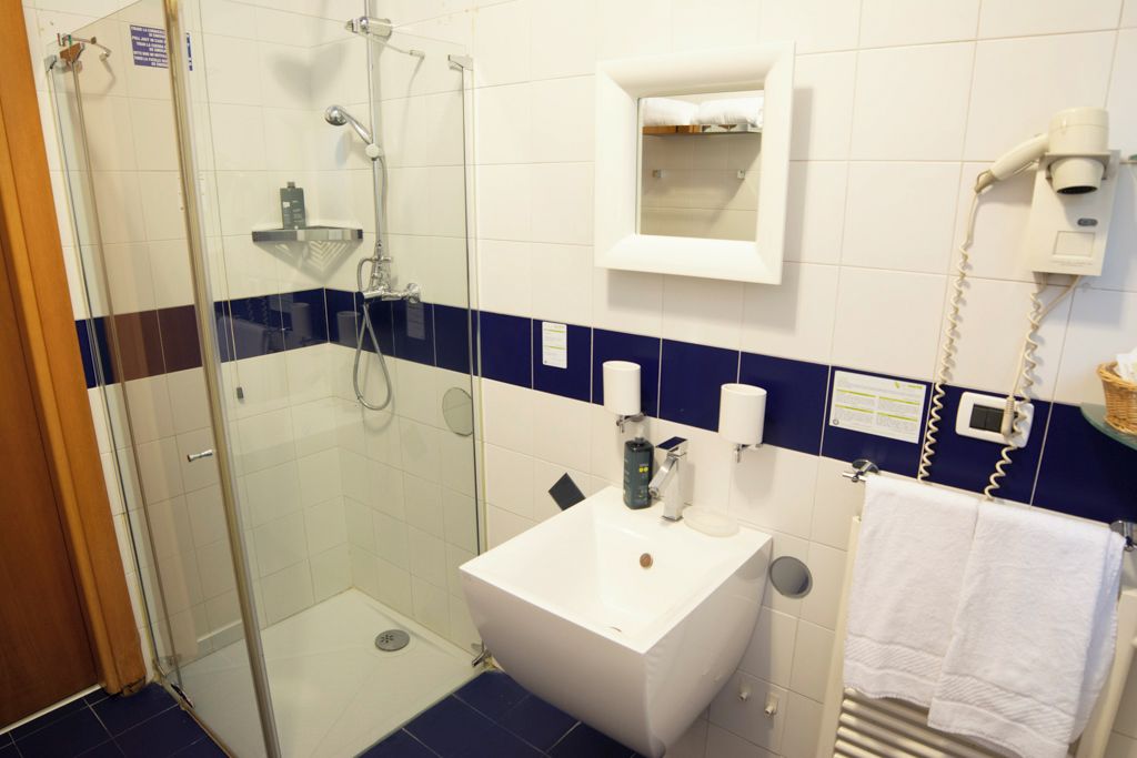 Un baño con cabina de ducha de vidrio, un lavabo blanco, un perchero y un espejo.