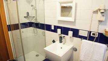 Un baño con cabina de ducha de vidrio, un lavabo blanco, un perchero y un espejo.