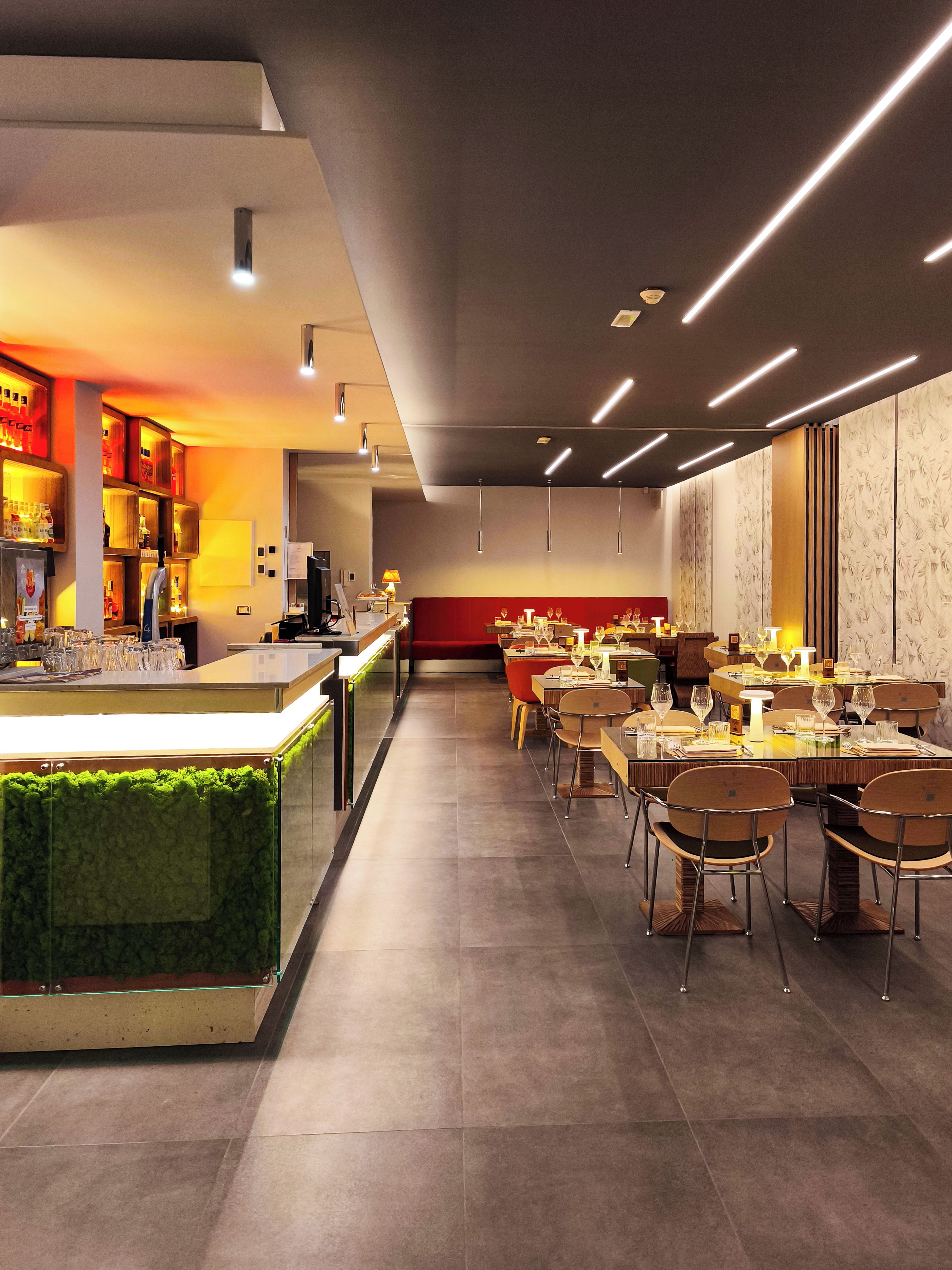 A modern restaurant interior with a bar area, dining tables, and chairs.