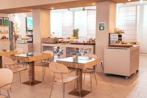 Un café moderno con mesas y sillas, una zona de bufé con comida y una barra con la carta.