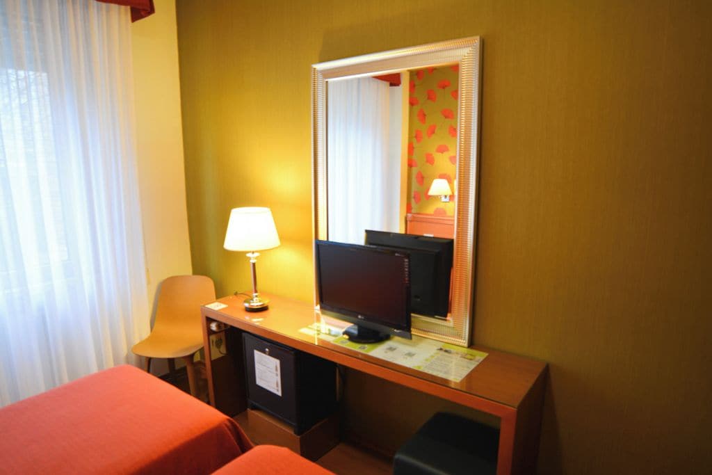 Een hotelkamer met een bureau, een computer, een stoel, een bed en een raam met gordijnen.