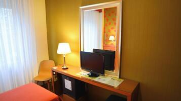 Een hotelkamer met een bureau, een computer, een stoel, een bed en een raam met gordijnen.