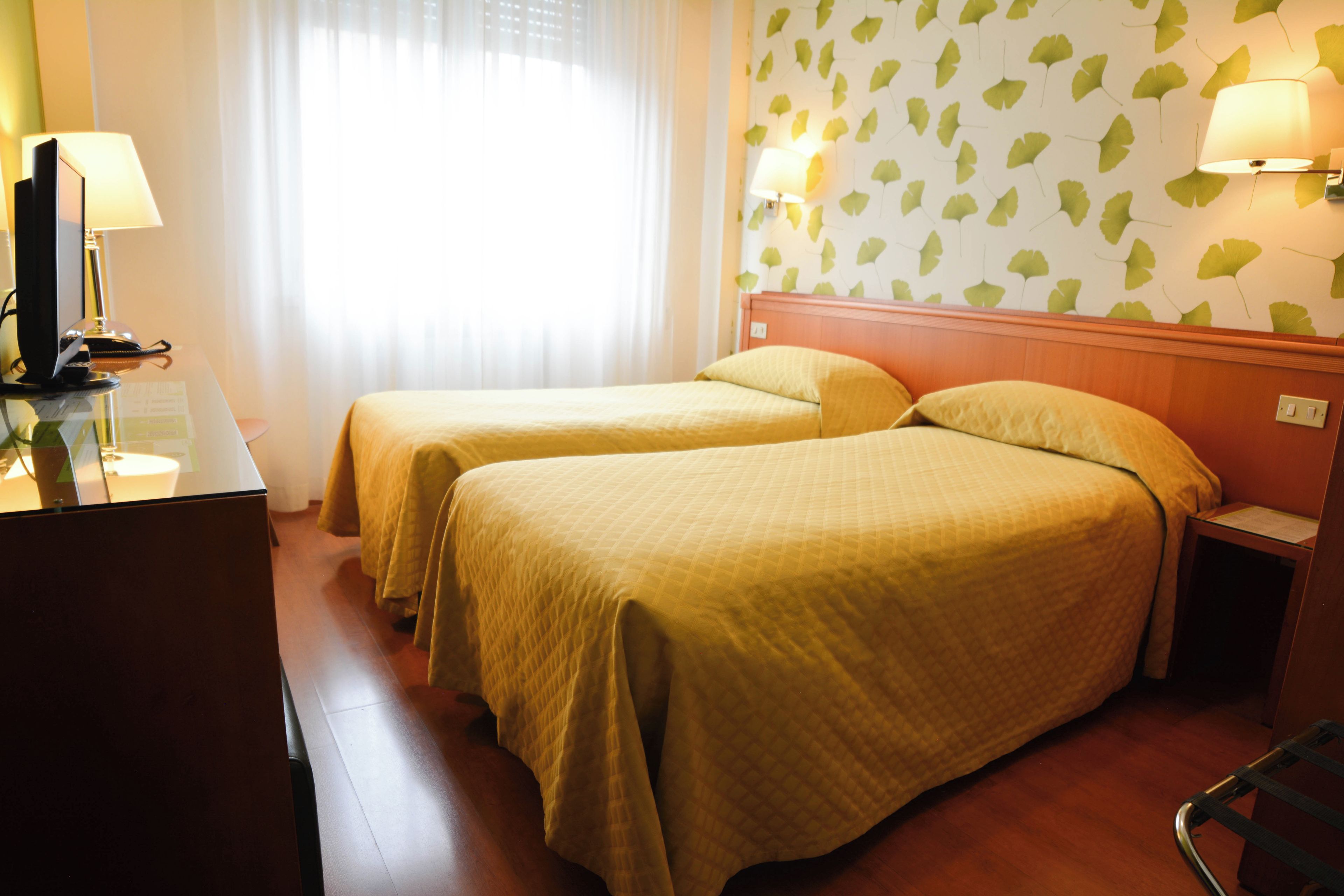 Habitación de hotel con dos camas, un escritorio con ordenador y una ventana con cortinas.