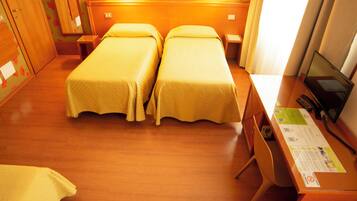 A hotel room with two single beds, a desk with a computer, and a television.