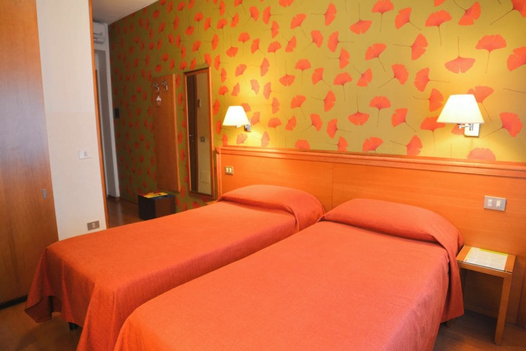 A hotel room with two beds, a wooden headboard, and a wall with a leaf pattern.