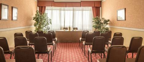 Un salón de conferencias con una larga mesa, varias sillas y dos plantas en macetas.